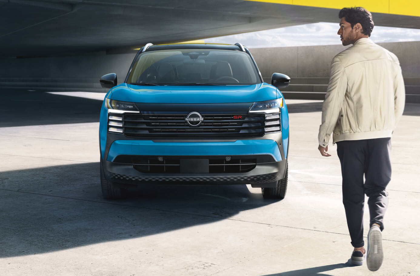 Front view of a Nissan Kicks SR in Blue Metallic parked as a man walks toward it under a bridge.