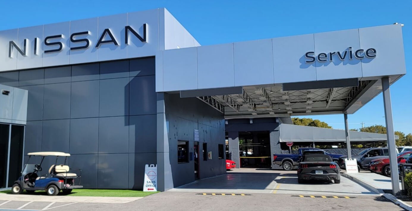 Exterior view of a modern Nissan dealership service drive under a blue sky with a golf cart parked.